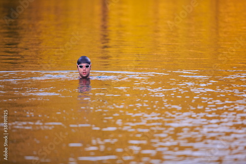 Fototapeta Naklejka Na Ścianę i Meble -  triathlon athlete swimming on lake in sunrise wearing wetsuit