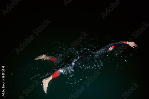 triathlon athlete swimming in dark night wearing wetsuit photo