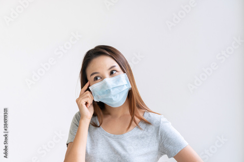 Portrait of happy charming young Asian girl with protective face mask and t shirt looks to the side, thinking and plan something. Isolated over white background. Copy space © Pattarisara