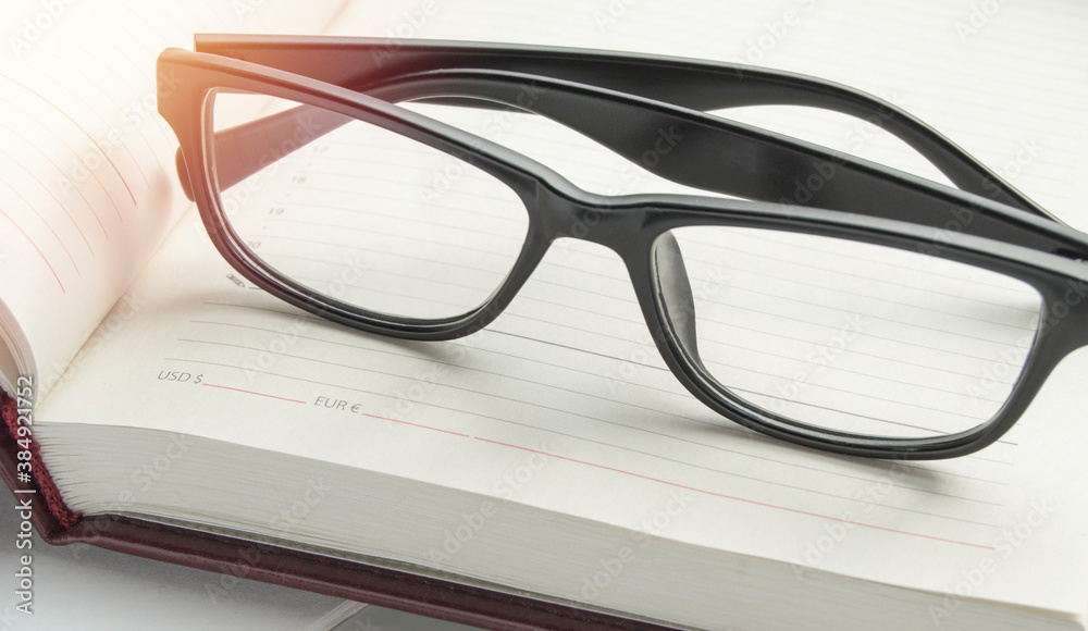 Stylish black reading glasses on an open diary, close-up banner