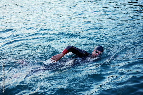triathlon athlete swimming on lake in sunrise wearing wetsuit