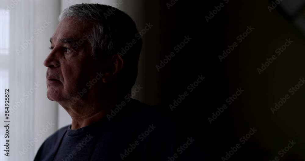 Thoughtful senior standing by window in meditation, good for transition Thoughtful senior standing by window in meditation, good for transition