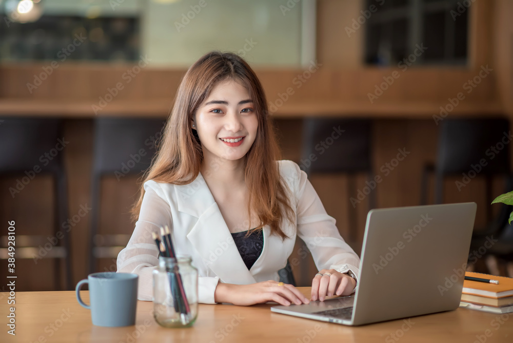 Young pretty asian businesswoman working on laptop while sitting at the table in office. Looking at camera.