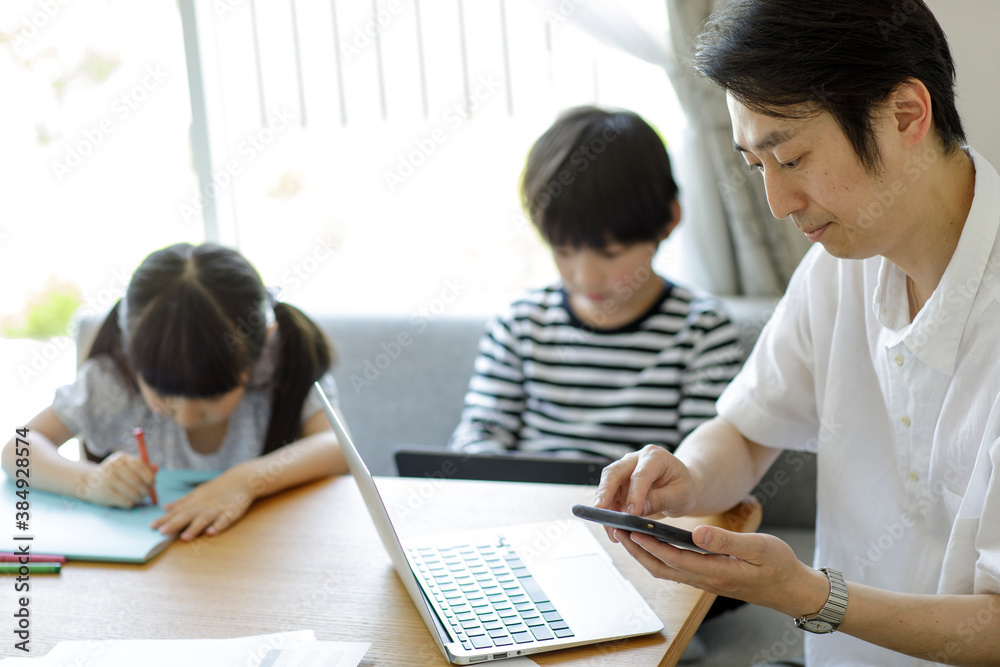テレワークをする父親とそばで遊ぶ子供たち テレワークをする父親とそばで遊ぶ子供たち