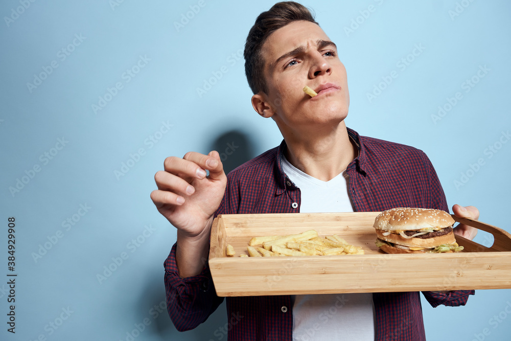 Man with wooden pallet fast food french fries hamburger hunger diet food blue background Man with wooden pallet fast food french fries hamburger hunger diet food blue background