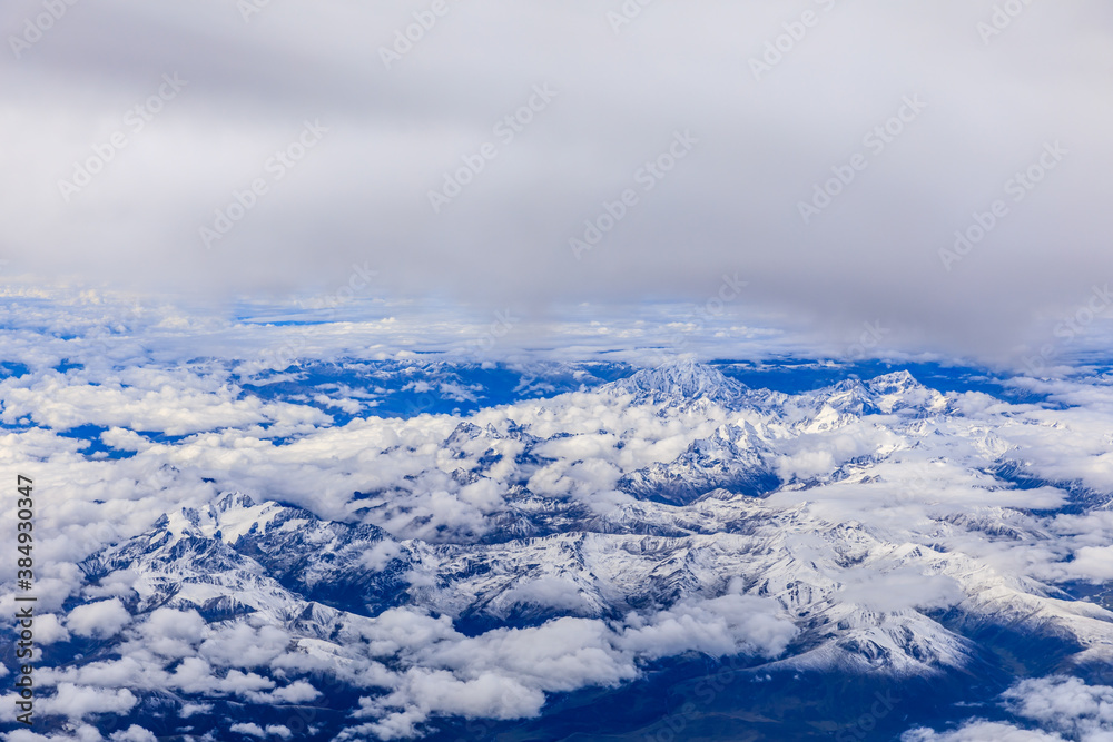 Aerial view above the clouds and misty mountain peaks covered with snow on a sunny day.China Tibet.