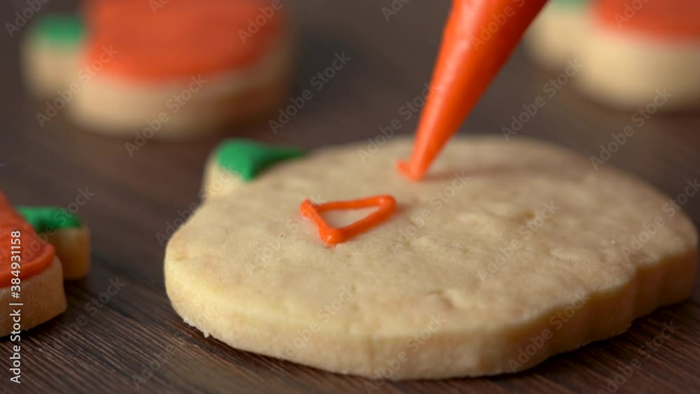 Close up of decorating cute Halloween pumpkin gingerbread cookies with frosting icing cream topping bag.
