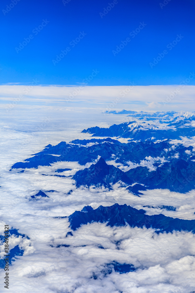 Obraz premium Aerial view above the clouds and mountain peaks on a sunny day.