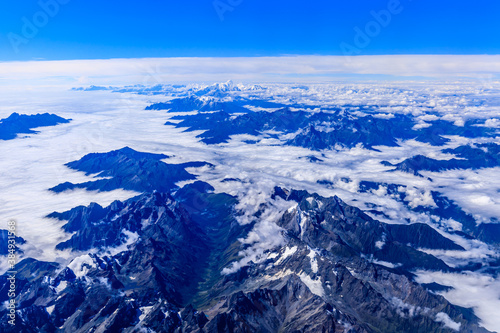 Aerial view above the clouds and mountain peaks on a sunny day.