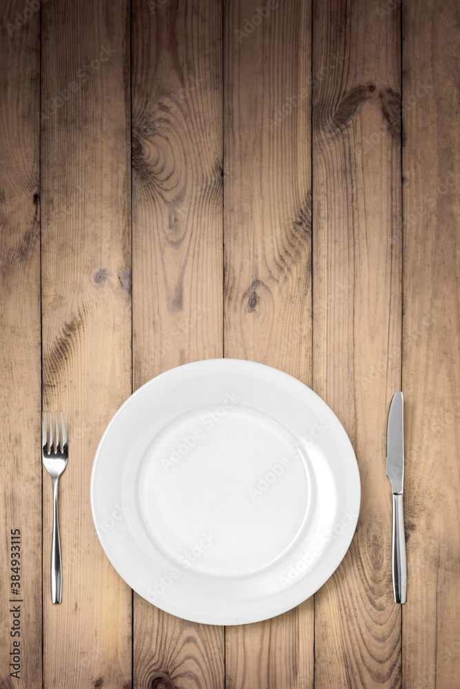 Empty white plate with knife and fork on a wooden table Empty white plate with knife and fork on a wooden table