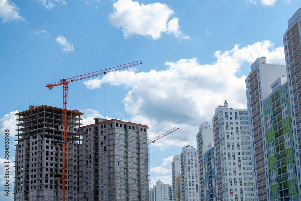 A multi-storey building under construction against the new bright finished residential buildings. High-rise cranes for the construction of new apartment buildings. Houses for purchase with a mortgage.