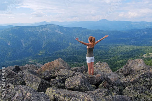 A woman jumps, dances, and climbs, does yoga on top of mountains. Young woman hiking up hill against a blue sky with clouds.