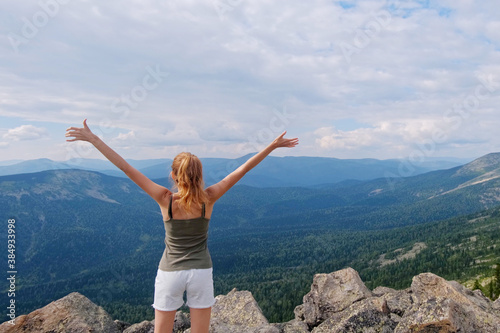 A woman jumps, dances, and climbs, does yoga on top of mountains. Young woman hiking up hill against a blue sky with clouds.