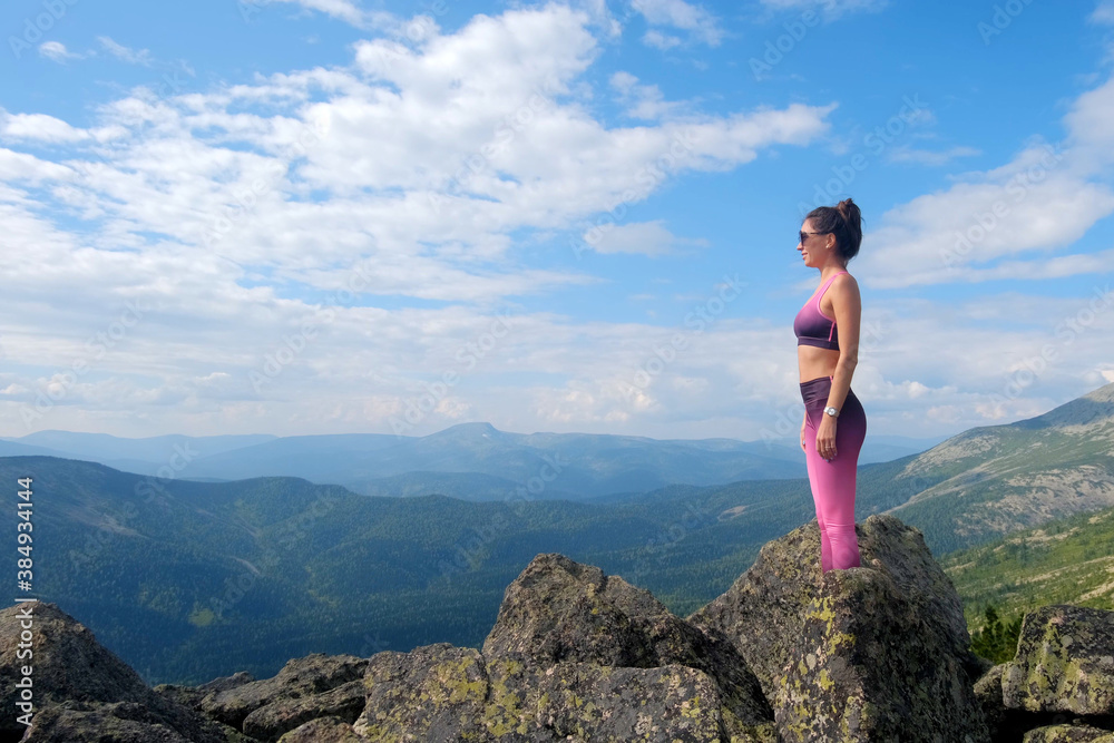 Naklejka premium Young woman hiking up hill against a blue sky with clouds. A woman jumps, dances, and climbs on top of mountains.