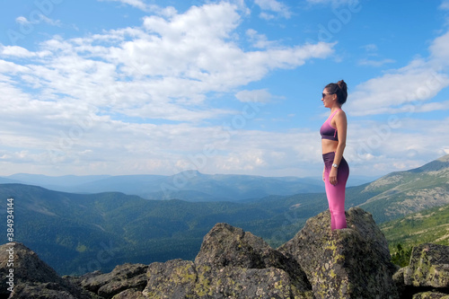 Young woman hiking up hill against a blue sky with clouds. A woman jumps, dances, and climbs on top of mountains.