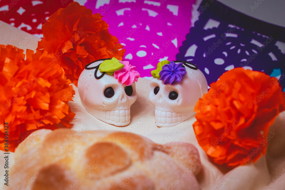 Day of the dead bread accompanied with a cup of coffee and white chocolate skulls with a traditional colorful background of the Day of the Dead