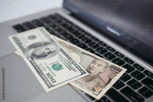 100ドル紙幣と一万円札とパソコン