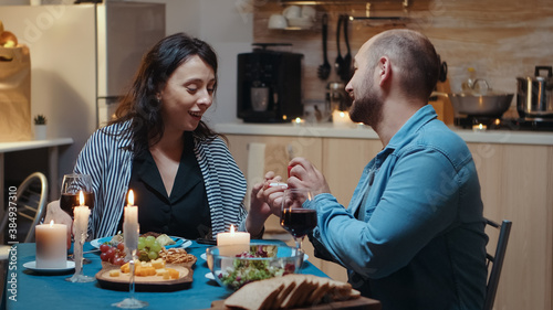 Young cheerful woman being surprised by marriage proposal of her husband. Man making proposal to his girlfriend in the kitchen during romantic dinner. Happy caucasian woman smiling being speechless