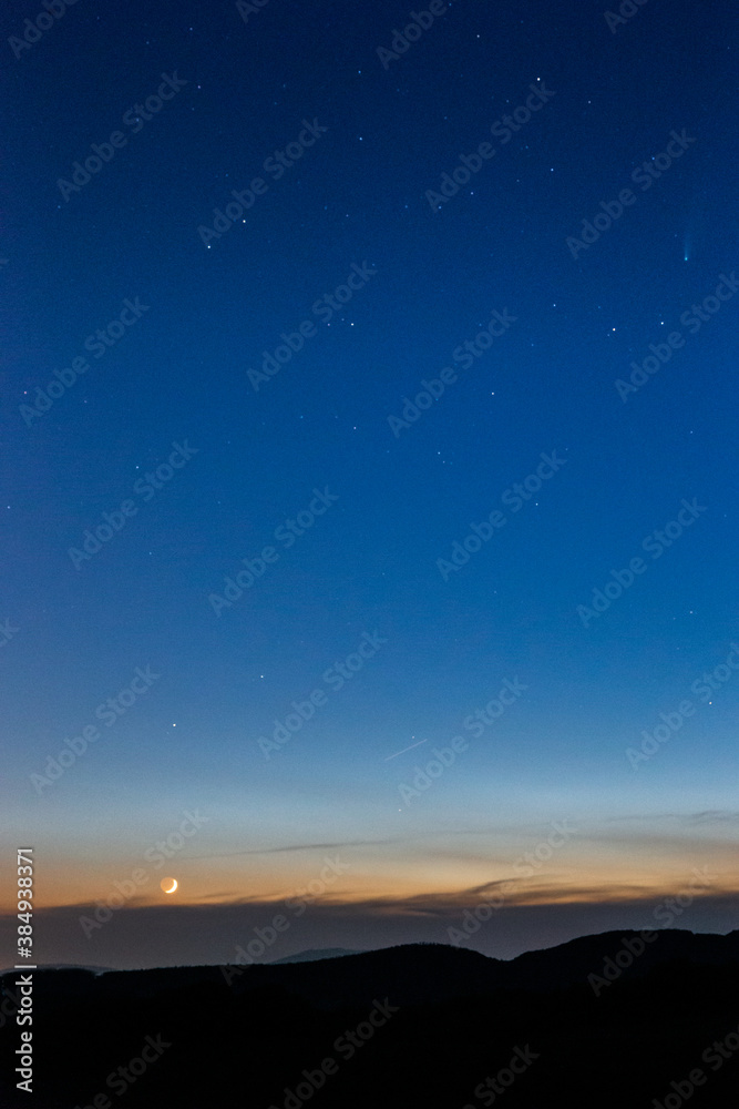 Moon and Neowise comet at dusk on a blue sky above mountains