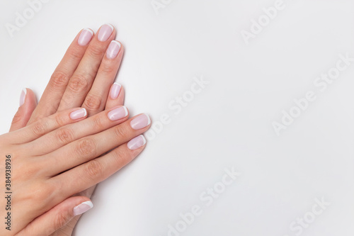 French manicure. Nude nails covered with gel polish on a white background with copy space. Natural manicure with camouflage base. Female hands close up, beauty salon concept © studiomay