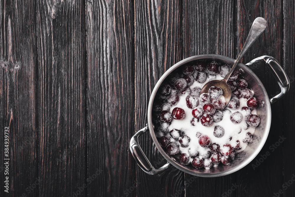 Pot with cherries and sugar on black wooden table, top view. Making of delicious jam