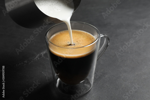 Pouring milk into cup of coffee on black table
