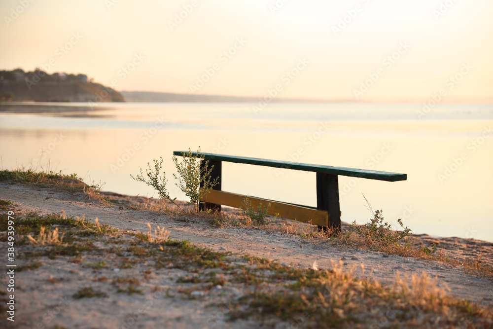 Wooden bench near river at sunrise. Early morning landscape