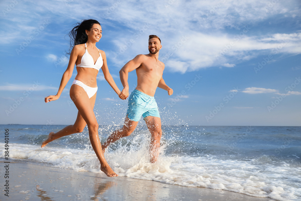 Happy young couple running together on beach - obrazy, fototapety, plakaty 