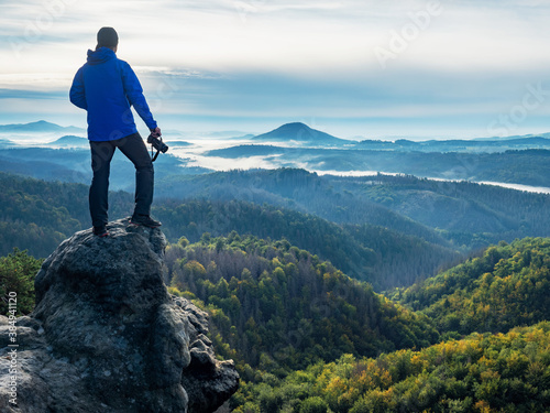 Camera in the hand of man tourist standing on rock above white mist valley photo