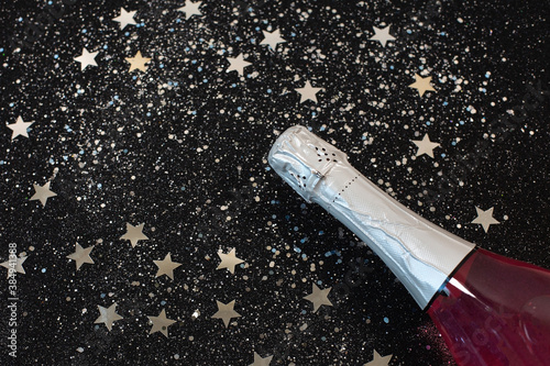 Bottle of champagne with star confetti lying on black background.
