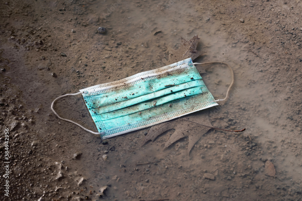 discarded used disposable face mask lying on ground in puddle - thrown away corona covid-19 masks becoming environmental littering problem discarded used disposable face mask lying on ground in puddle - thrown away corona covid-19 masks becoming environmental littering problem
