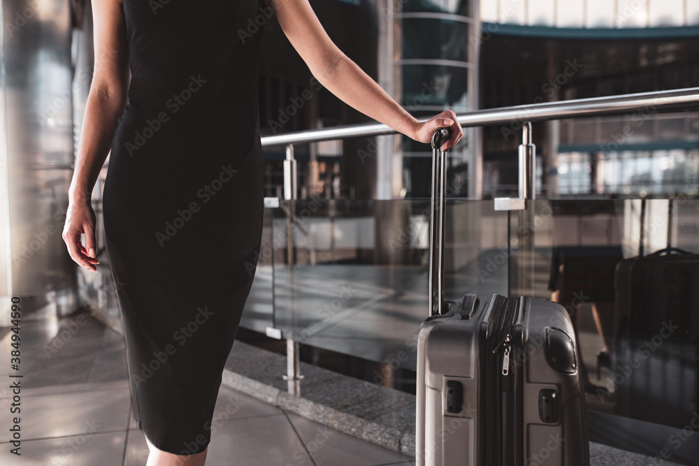 Woman wearing a black dress and holding a convenient suitcase