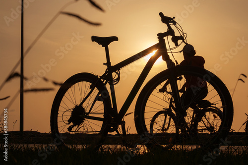 The sun shines through the frame of a bicycle with silhouette of bicycle rider at background