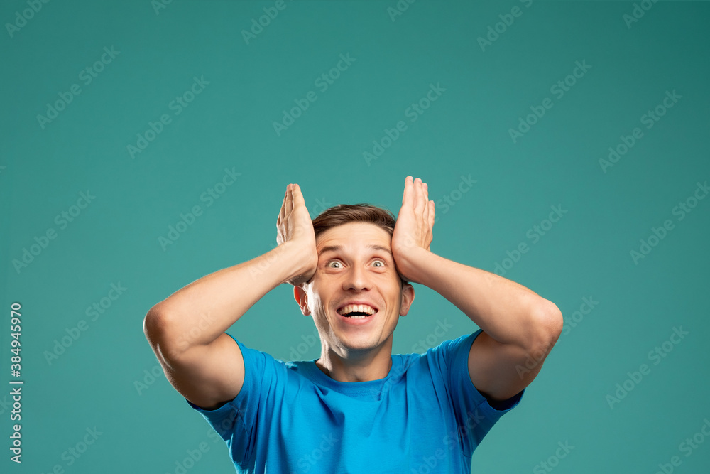 Unbelievable success. Great achievement. Euphoric emotion. Got it. Expected result. Invisible message. Excited young man holding head looking up copy space isolated on blue. Unbelievable success. Great achievement. Euphoric emotion. Got it. Expected result. Invisible message. Excited young man holding head looking up copy space isolated on blue.