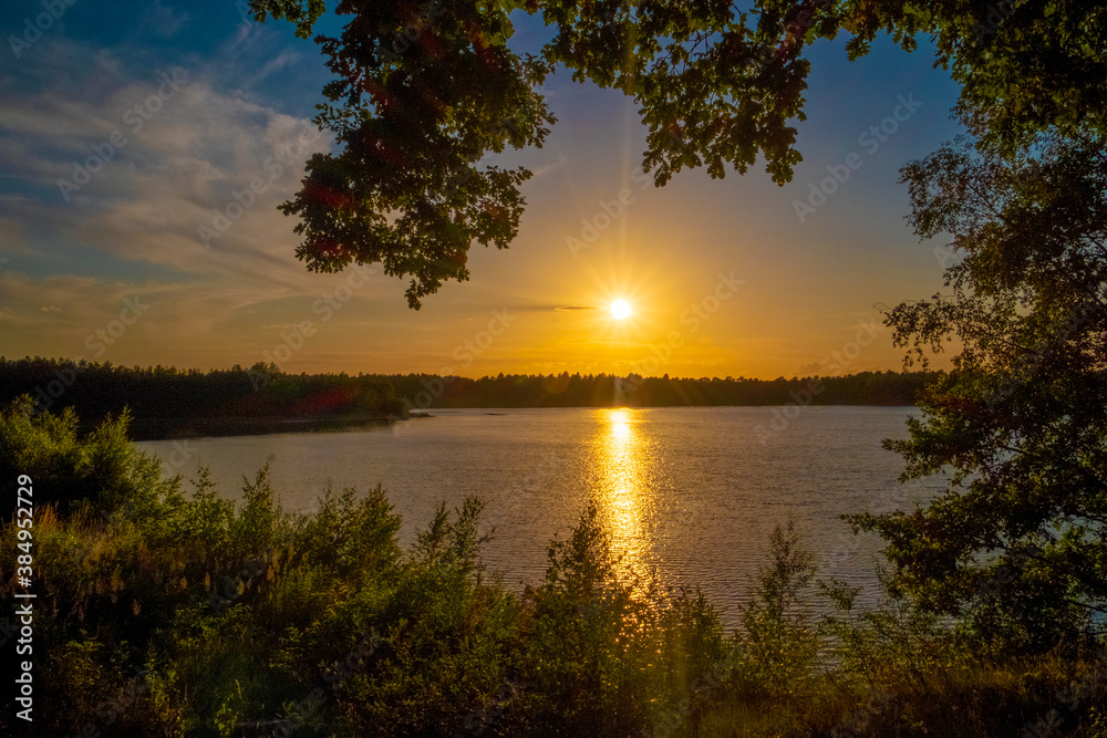 Panorama of a gorgeous sunset at a forest lake, with gold and blue color in the sky and trees reflected in the water. High quality photo