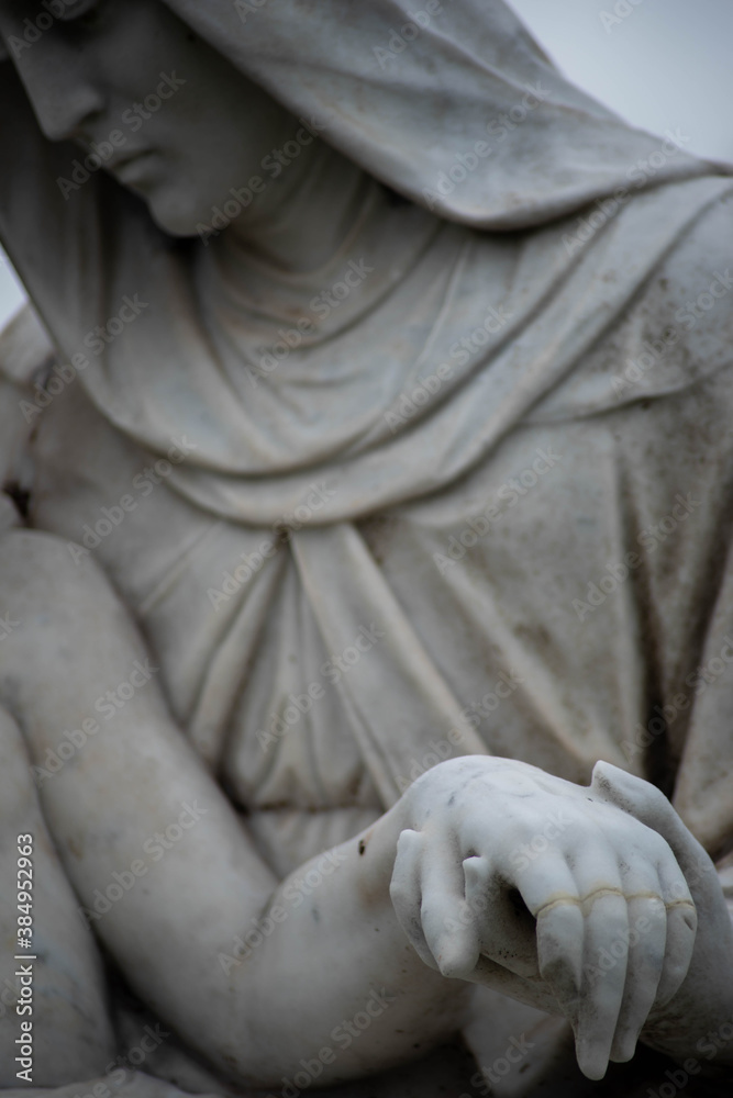 Beautiful stone pieta in a Victorian cemetery. Full frame image in natural light. Selective focus on joined hands.