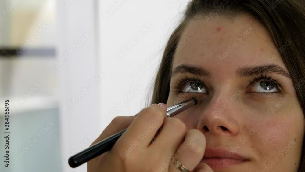 Attractive female face of a brunette well-groomed woman. Makeup artist applies eye shadows to the eyelid of the model eyes. Portrait of a beautiful young woman. Professional stylish makeup. Attractive female face of a brunette well-groomed woman. Makeup artist applies eye shadows to the eyelid of the model eyes. Portrait of a beautiful young woman. Professional stylish makeup.