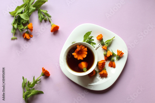 Calendula flowers with a Cup of medicinal tea in a white dish on a purple background, top view