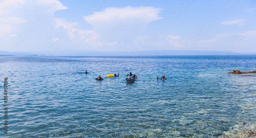 Scuba diver with oxygen tank preparing for diving entering in the beautiful Greece turquoise sea. Summer holiday activity.
