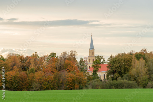 church in autumn. Trees with orange leaves and a green field in the foreground