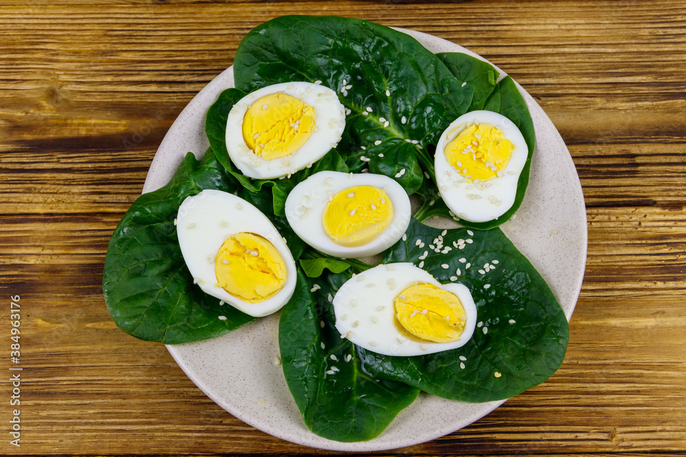 Boiled eggs with fresh spinach leaves and sesame seeds on wooden table. Top view Boiled eggs with fresh spinach leaves and sesame seeds on wooden table. Top view
