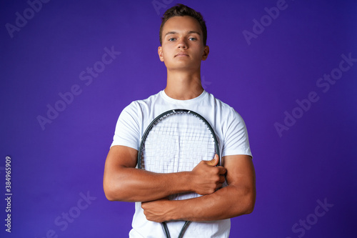 Caucasian young man tennis player posing with tennis racket against purple background © fotofabrika