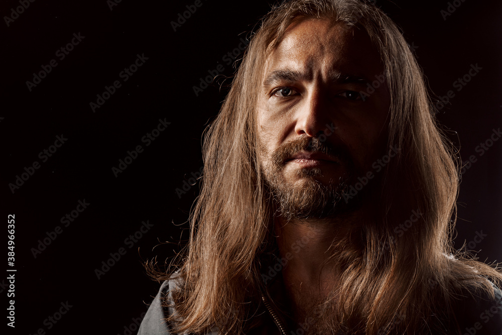 Long-haired masculine middle-aged man standing in the dark