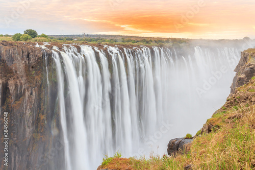 Victoria Falls, a waterfall in southern Africa on the Zambezi River at the border between Zambia and Zimbabwe. Milky water & orange clouds
