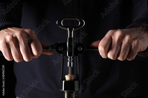 close up on two man's hands opening a wine bottle with opener on black background