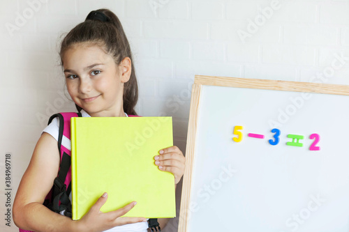 Happy school girl with book near blackboard