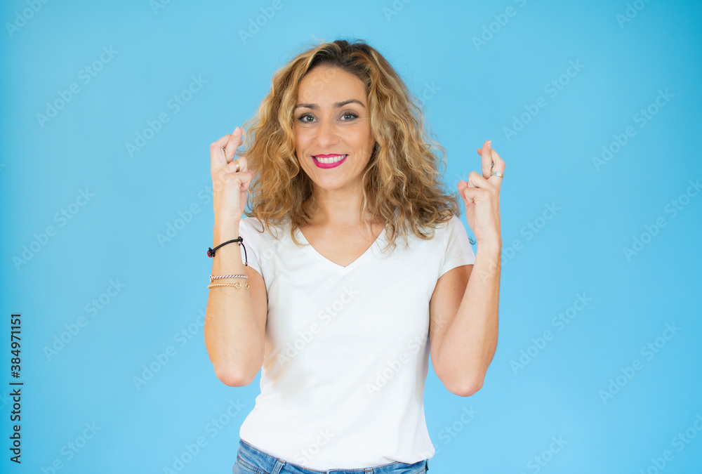 Fototapeta premium Beautiful woman with curly hair wearing white casual t-shirt over isolated background gesturing finger crossed smiling with hope. Luck and superstitious concept.