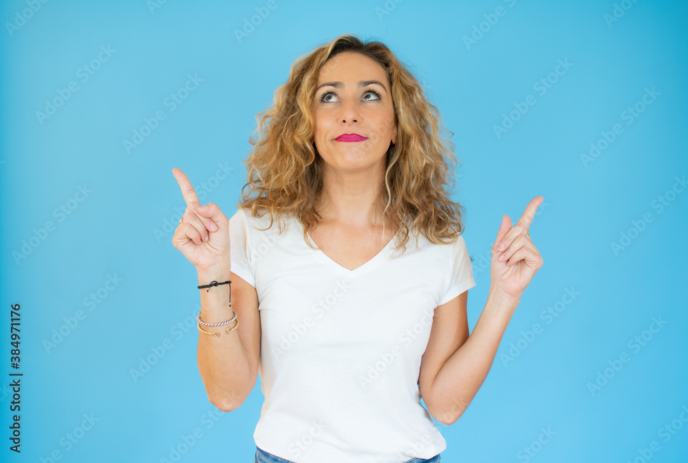 Beautiful blonde woman over blue background showing and pointing up with finger number one while smiling confident and happy. Beautiful blonde woman over blue background showing and pointing up with finger number one while smiling confident and happy.