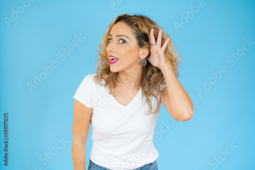 Young pretty woman wearing white t-shirt smiling with hand over ear listening an hearing to rumor or gossip. Deafness concept.