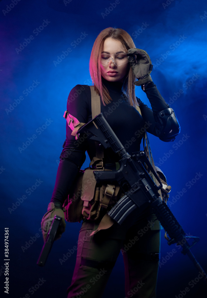 a woman in military airsoft uniform with an American automatic rifle and pistol on a dark background